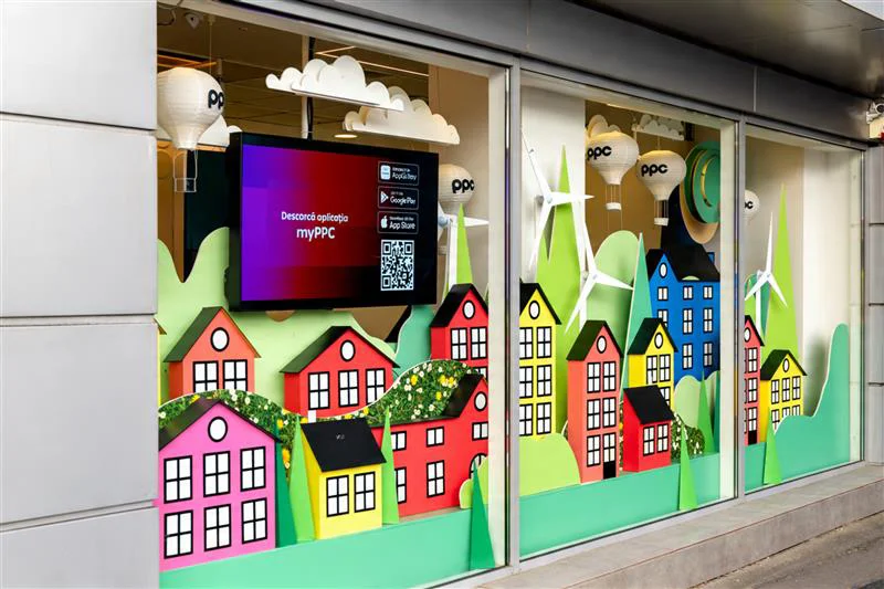 Vitrină magazin PPC Brașov decorată cu căsuțe colorate, turbine eoliene și baloane cu aer cald pentru atelierele de copii